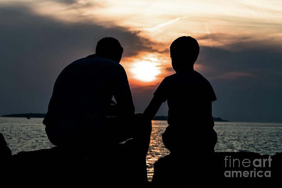 Father And Son Talking While Sitting On Stones At The Coast During Sunset Photograph by Andreas Berthold