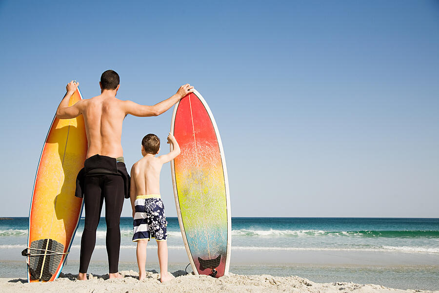 Father and son with surfboards gazing out to sea Photograph by Image Source