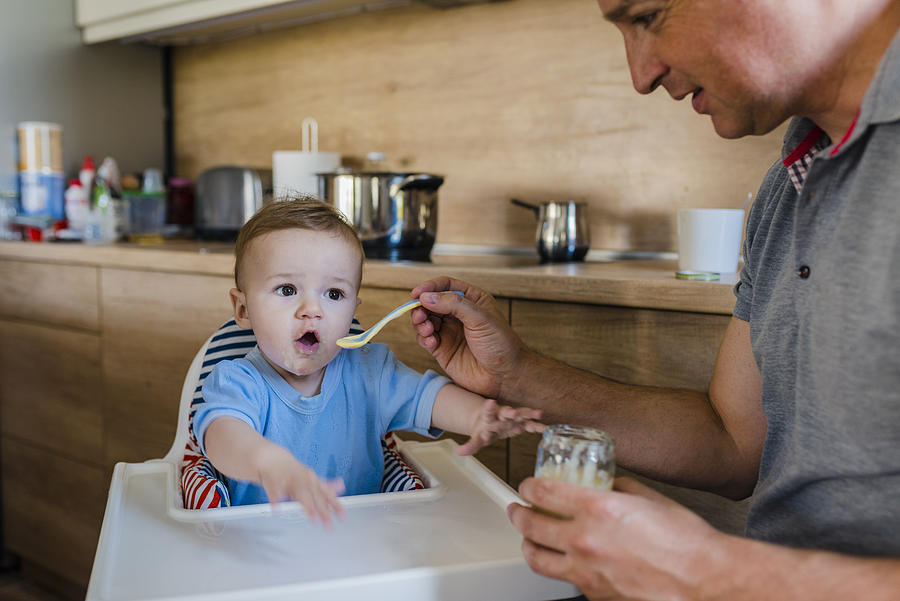 Father at home feeding his little son with yogurt Photograph by Ljubaphoto