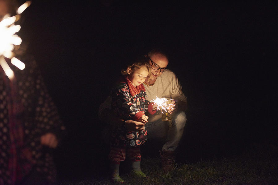 Father crouching next to daughter holding sparkler Photograph by J J D