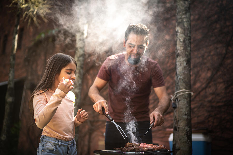 Father cutting a slice of meat to his daughter during a barbecue Photograph by FG Trade