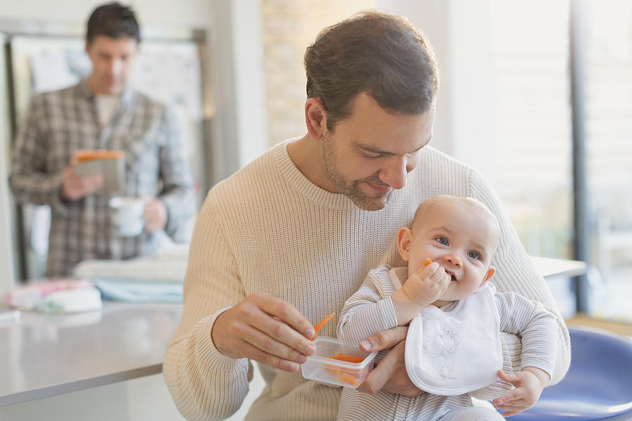 Father feeding carrots to baby son Photograph by Caia Image