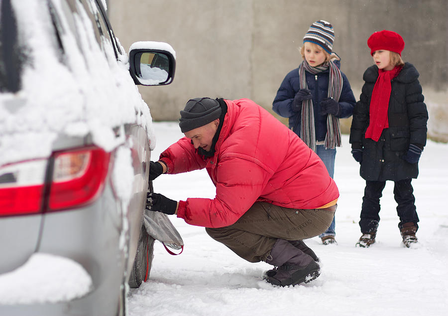Father fitting a snow sock on family car Photograph by Anne Heaton-Ward