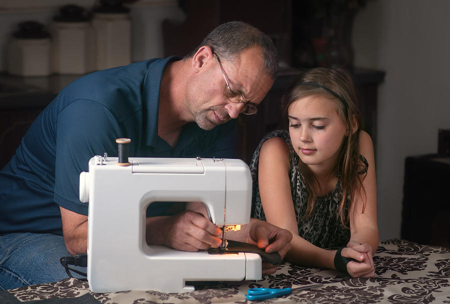 Father helping with his daughters sewing project. Photograph by Harpazo_hope