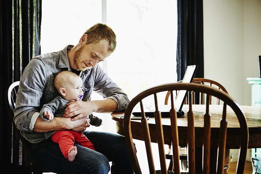 Father holding baby girl on lap at dining table Photograph by Thomas Barwick