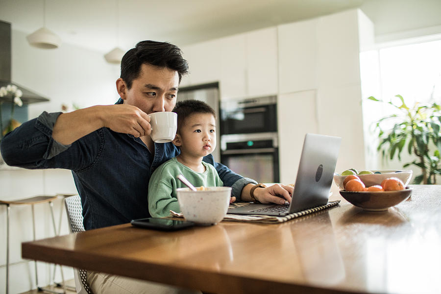 Father multi-tasking with young son (2 yrs) at kitchen table Photograph by MoMo Productions