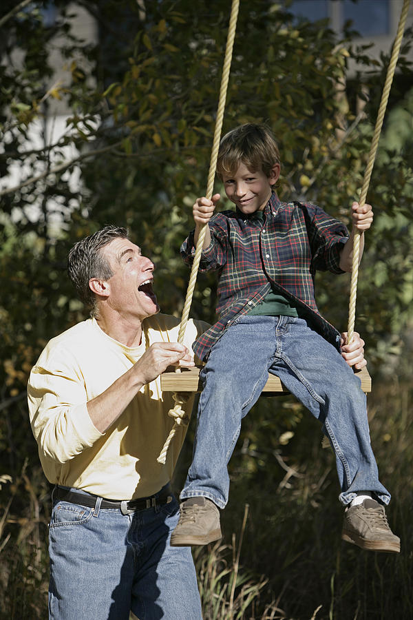 Father pushing son on a swing Photograph by Comstock Images