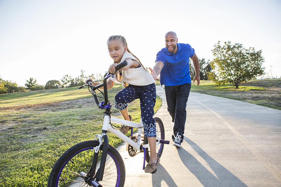 Father teaching daughter to ride bicycle in park Photograph by Sam Diephuis
