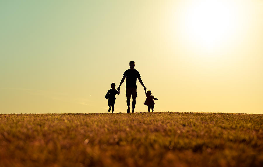 Father walking with son and daughter in park at sunset. Photograph by Kieferpix