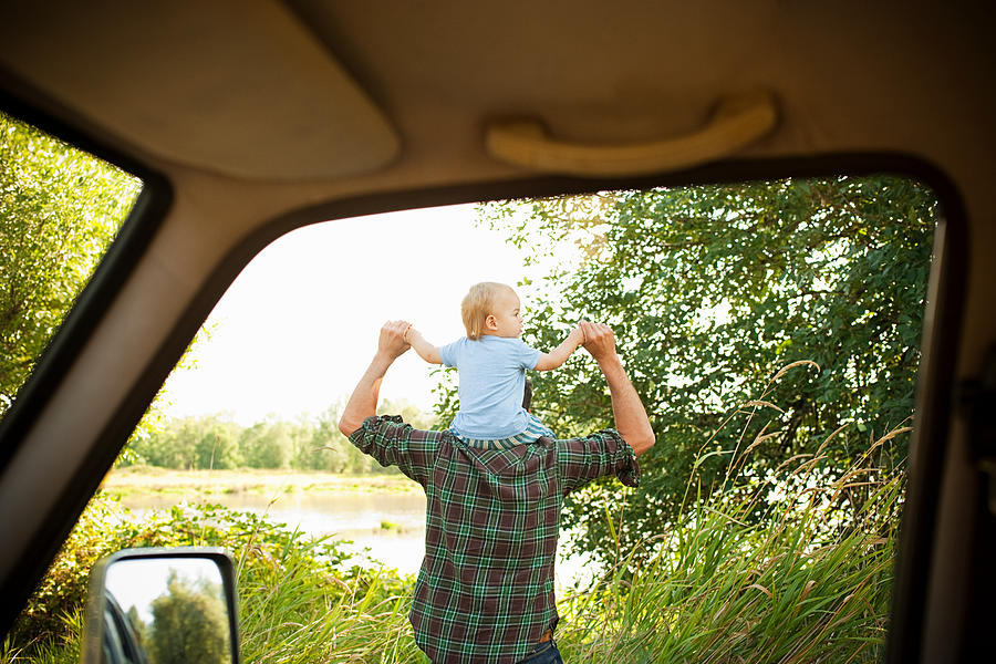 Father with son on shoulders, viewed from a car Photograph by Image Source