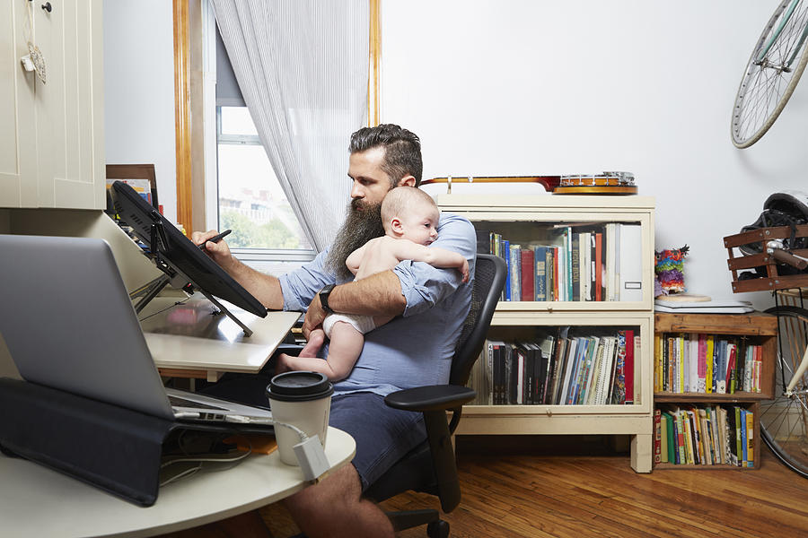 Father working from home while holding baby Photograph by Camille Tokerud