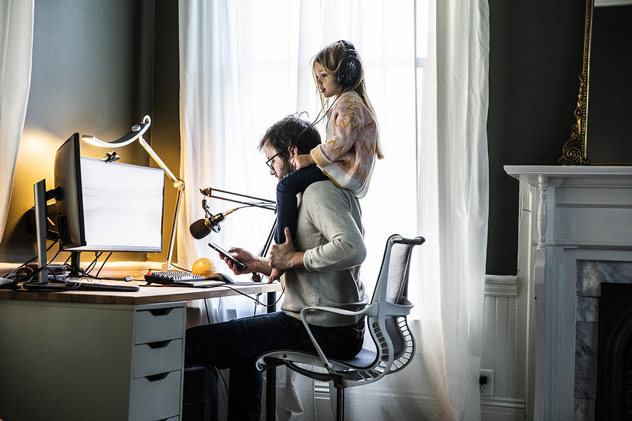 Father working in home office with  young daughter on shoulders Photograph by MoMo Productions