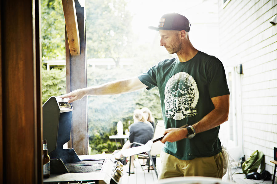 Father working on barbecue in backyard Photograph by Thomas Barwick