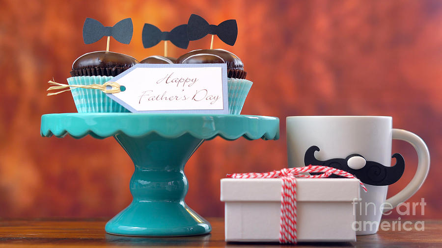 Fathers Day close up of gift, cupcakes and coffee mug against wood background. Photograph by Milleflore Images