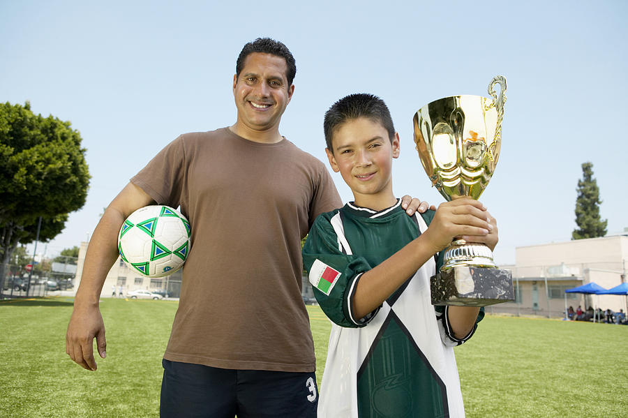 Fathers hand on sons (7-9) shoulder, boy holding trophy, portrait Photograph by Barry Austin Photography