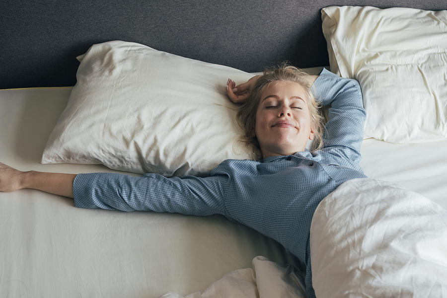 Feeling Energized: Happy Blonde Woman in Pyjamas Stretches in Bed after Waking Up in the Morning Photograph by FreshSplash