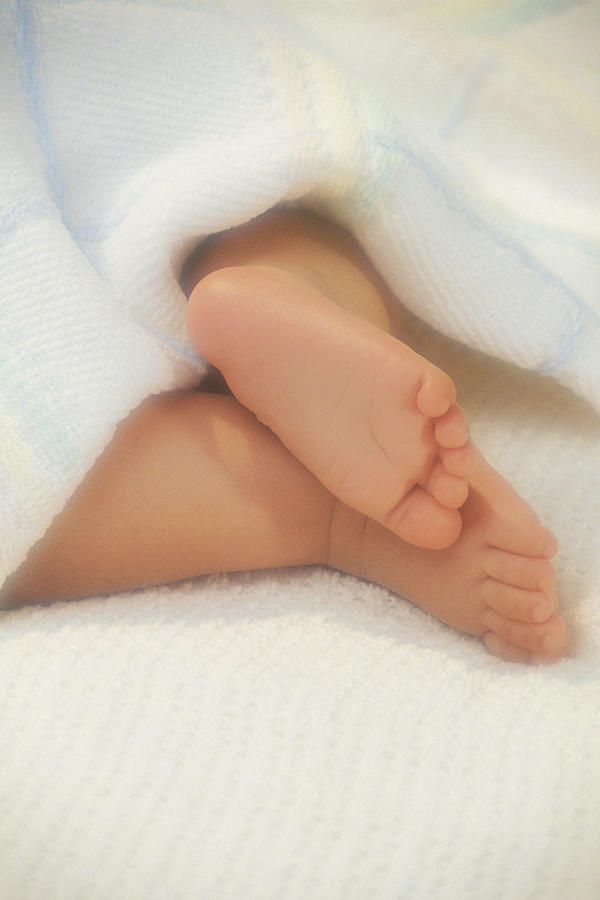 Feet of baby sticking out from under blanket Photograph by Comstock