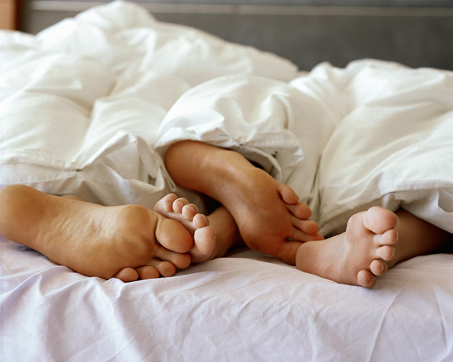 Feet of couple sticking out from under duvet, close up Photograph by Gallo Images-Hayley Baxter