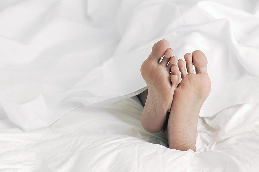 Feet under sheets Photograph by Comstock Images