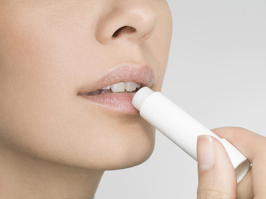 Female applying lip balm, close up, side view Photograph by Jonathan Knowles