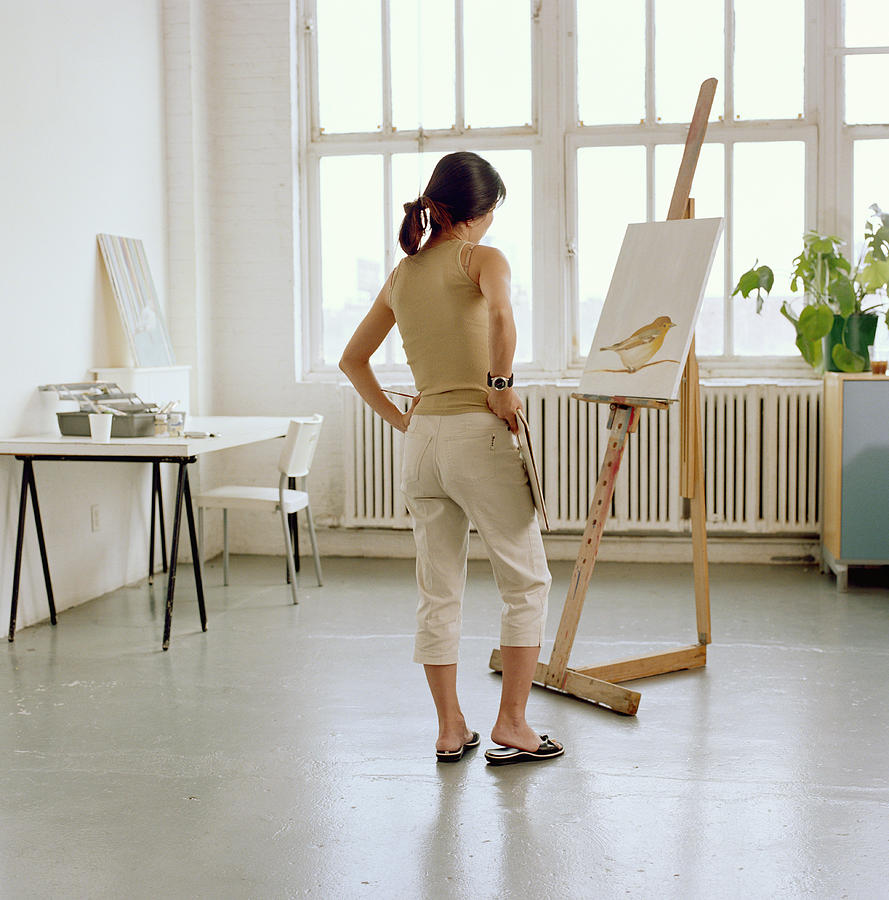 Female artist looking at painting on easel, rear view Photograph by Sean De Burca