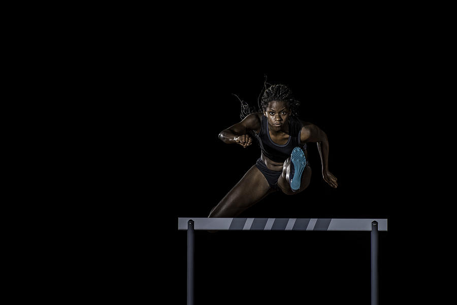 Female athlete jumping over a hurdle Photograph by Vm
