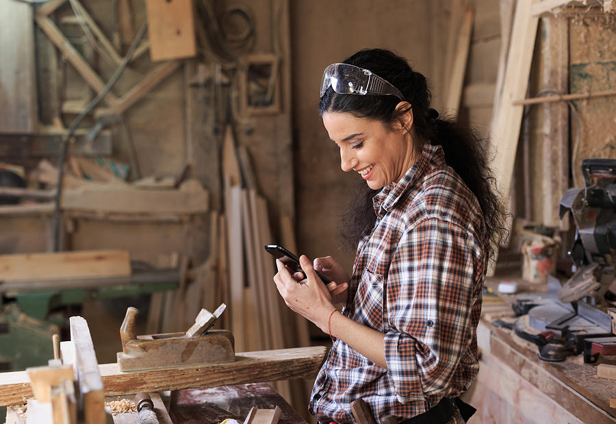Female carpenter using a phone at workhop Photograph by Valentinrussanov