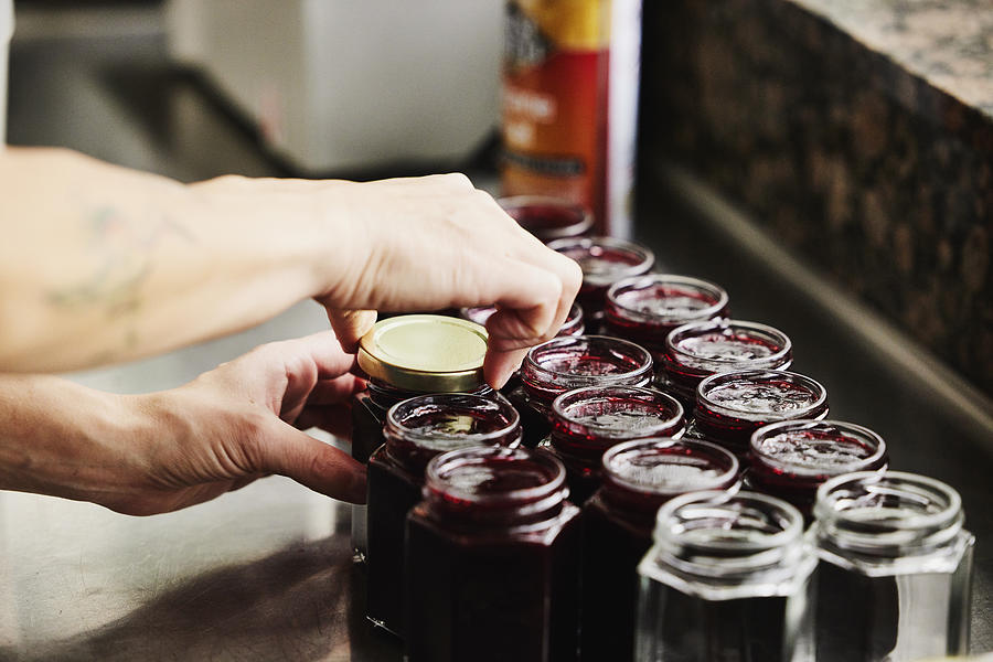 Female chef putting lids on jars of freshly made organic jam Photograph by Thomas Barwick