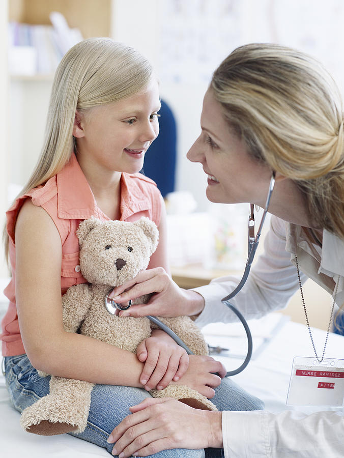 Female doctor examining girl with teddy bear Photograph by Chris Ryan