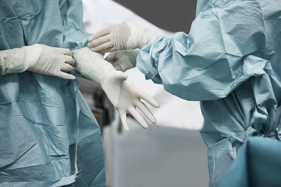 Female doctor helping surgeon wearing glove Photograph by Morsa Images