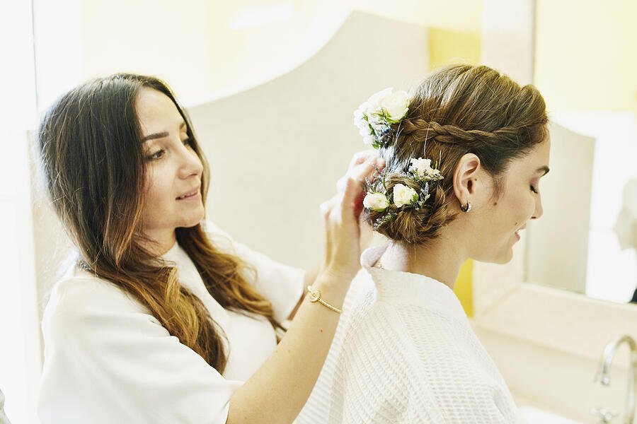 Female friend helping bride put flowers in hair before wedding Photograph by Thomas Barwick