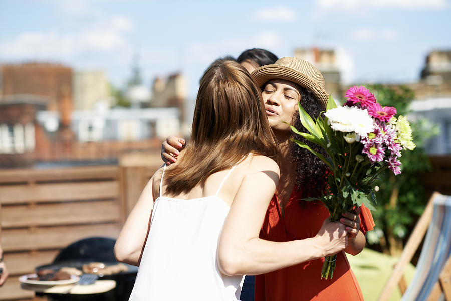 Female friends greeting with flower bouquet at rooftop barbecue Photograph by Peter Muller