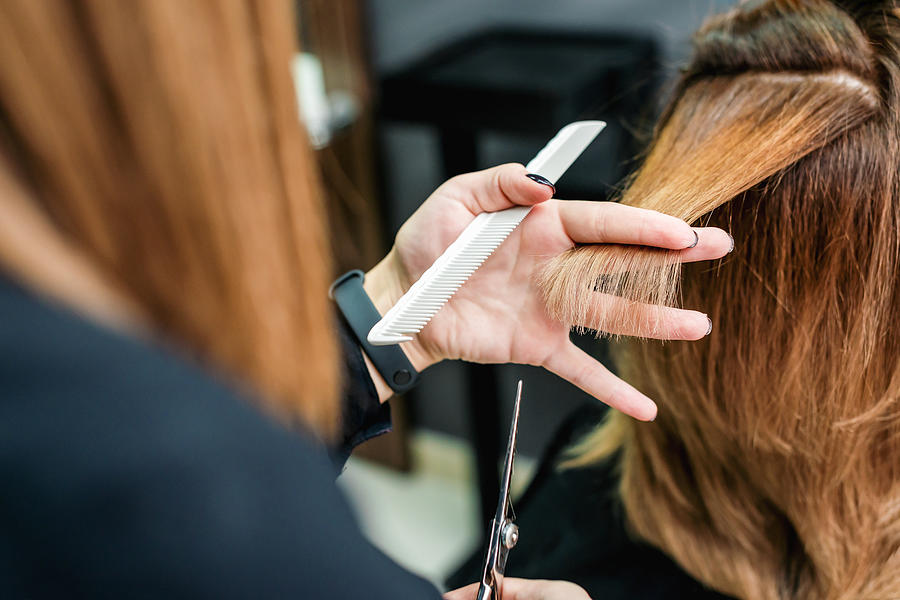 Female hairdresser is cutting woman hair close up. Photograph by Okskukuruza