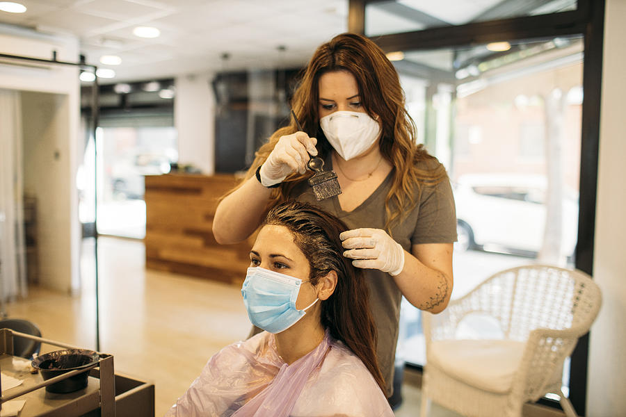Female hairdresser with mask staining hair of female customer with mask Photograph by Westend61