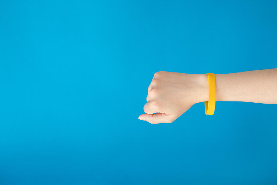 Female hand with empty yellow bracelet on blue background.  Clear sweat band mock up design. Photograph by Viktoriya Abdullina