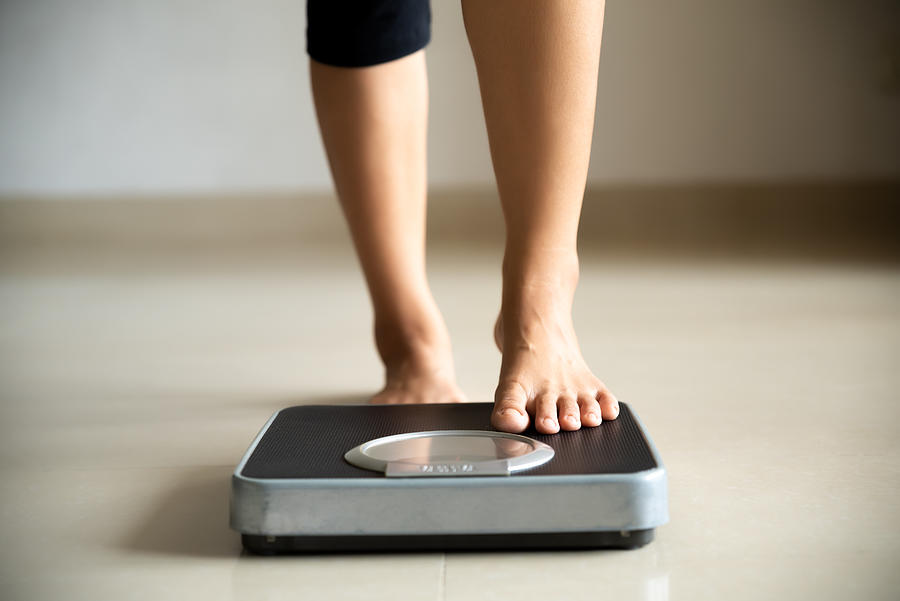 Female leg stepping on weigh scales. Healthy lifestyle, food and sport concept. Photograph by Spukkato