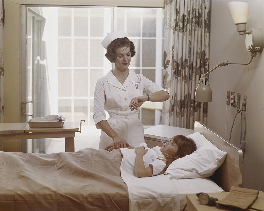 Female nurse checking pulse of girl in bed Photograph by Tom Kelley Archive