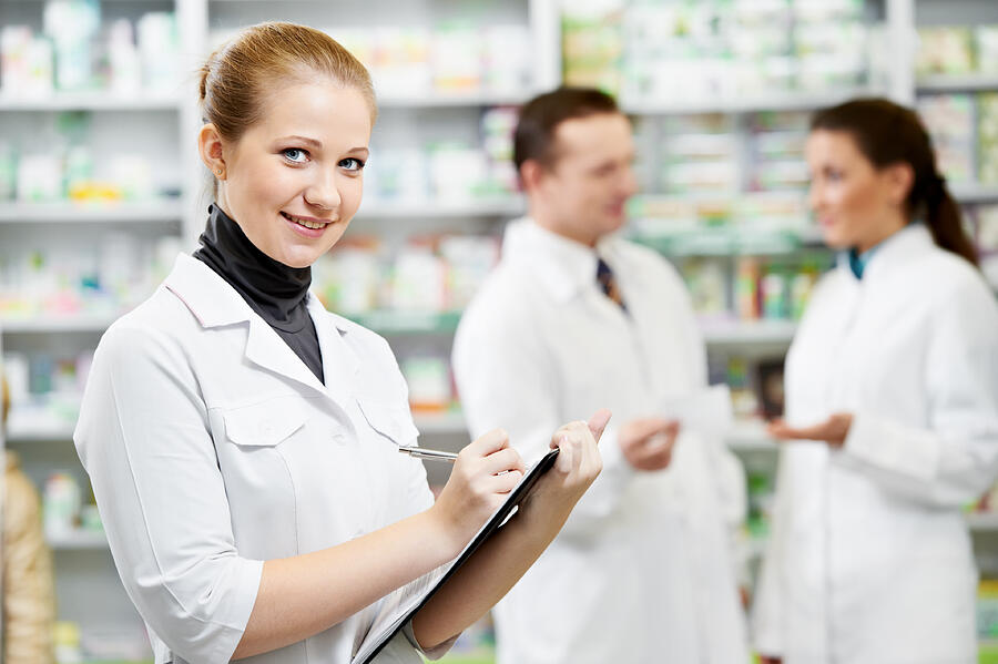 Female pharmacy technician with two others in background Photograph by Kadmy