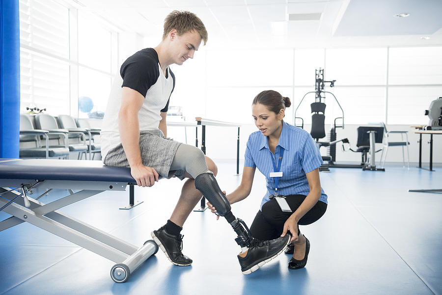 Female physiotherapist helping young man with prosthetic leg Photograph by JohnnyGreig