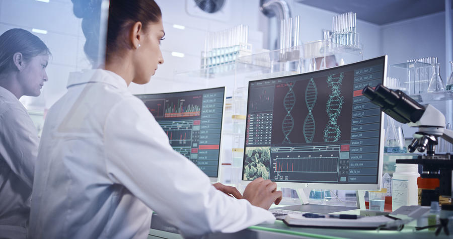 Female research team studying DNA mutations. Computer screens with DNA helix in foreground Photograph by Janiecbros