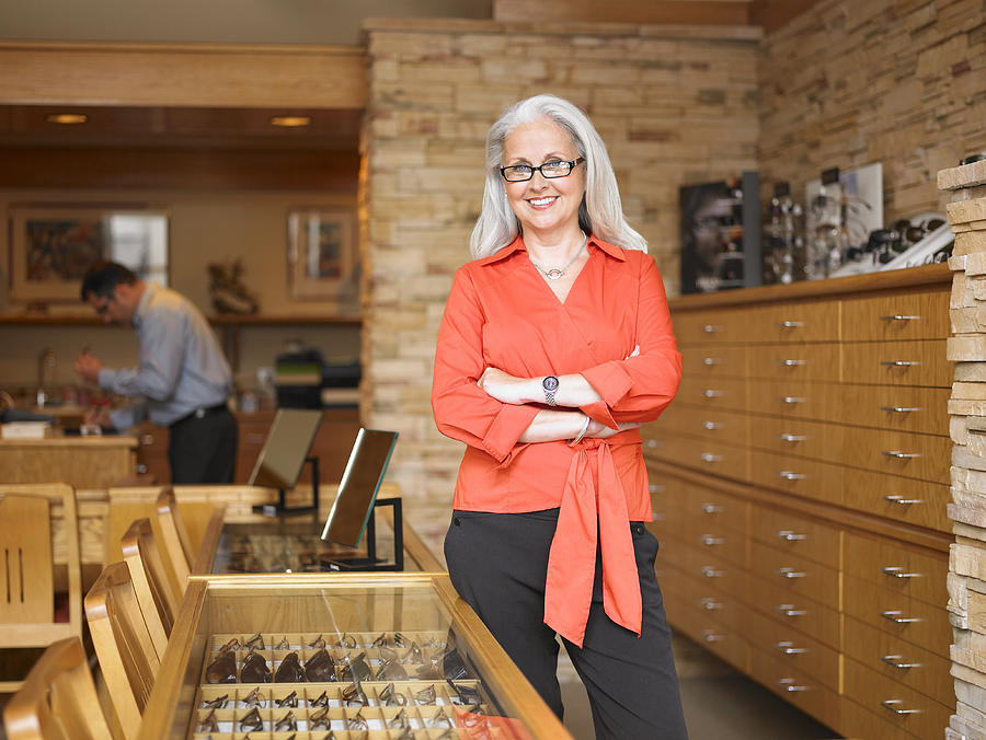 Female sales clerk standing in eyeglass store, portrait, customer in background Photograph by Siri Stafford
