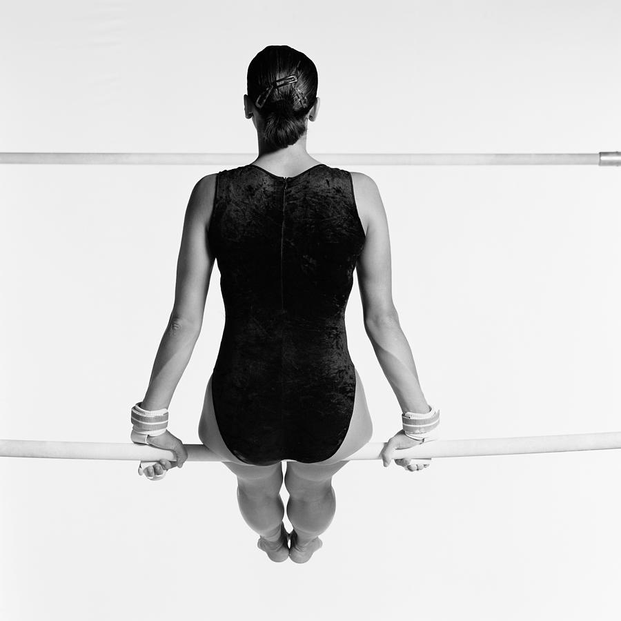 Female sitting on uneven bars, rear view, b&w. Photograph by Dominique Douieb