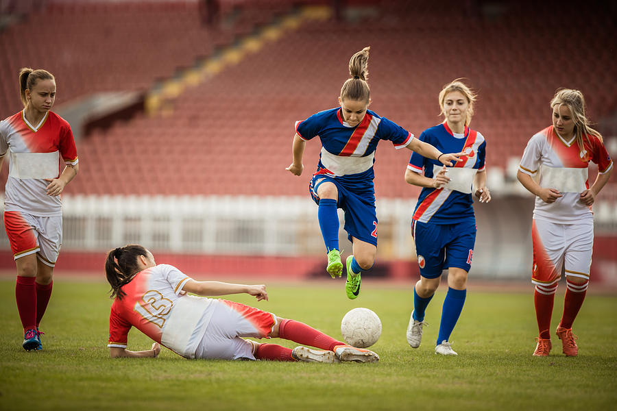 Female soccer player jumping over her opponent during a match on a stadium. Photograph by Skynesher