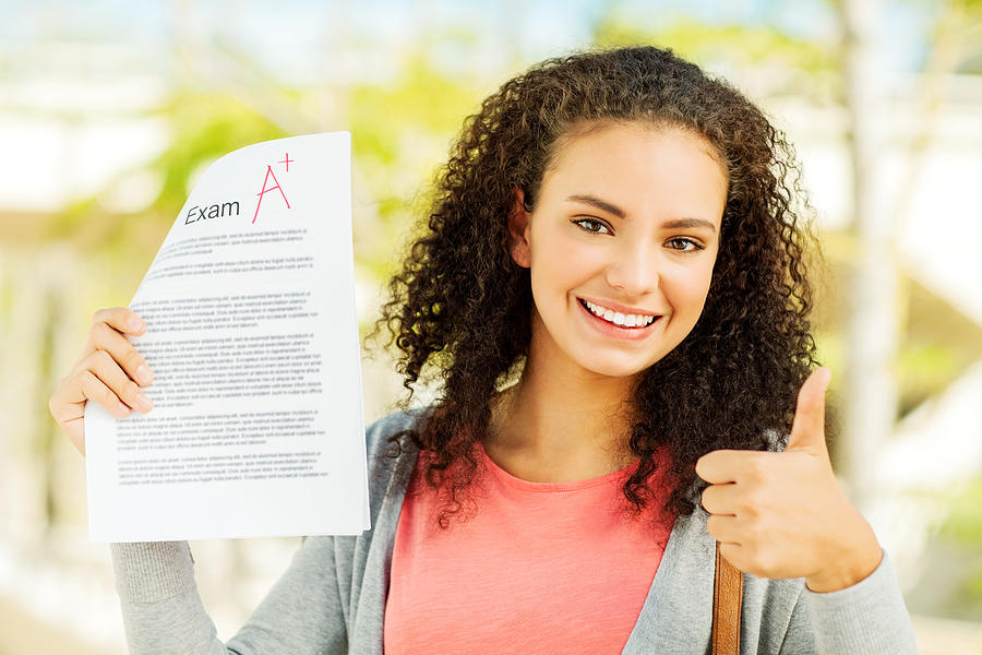 Female Student Gesturing Thumbs Up While Holding A Exam Result Photograph by Neustockimages