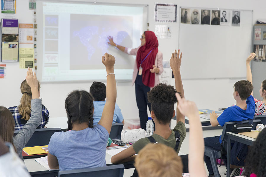 Female teacher in hijab teaching lesson at projection screen in classroom Photograph by Caia Image
