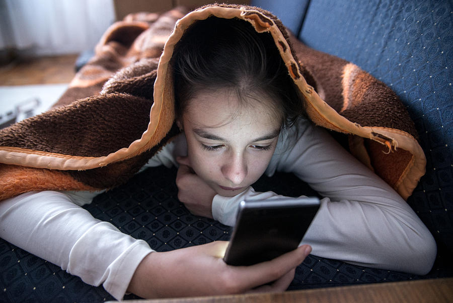 Female teen using phone in bed during the day Photograph by Ljubaphoto