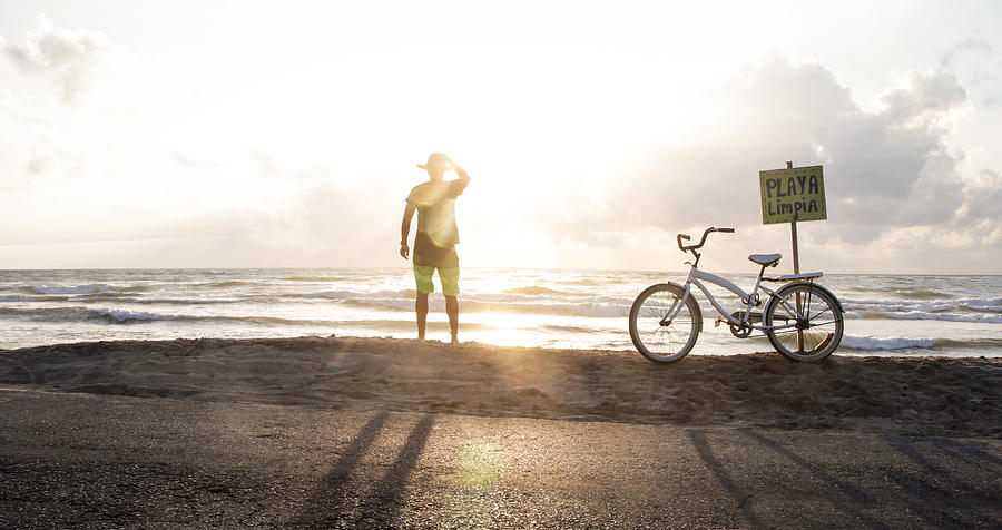 Female tourist with bike stops to watch sunrise over the ocean. Photograph by Gary John Norman