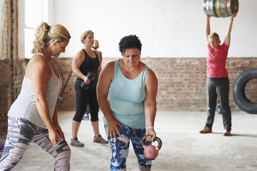 Female trainer working with woman lifting kettlebell in the gym Photograph by Richard Drury