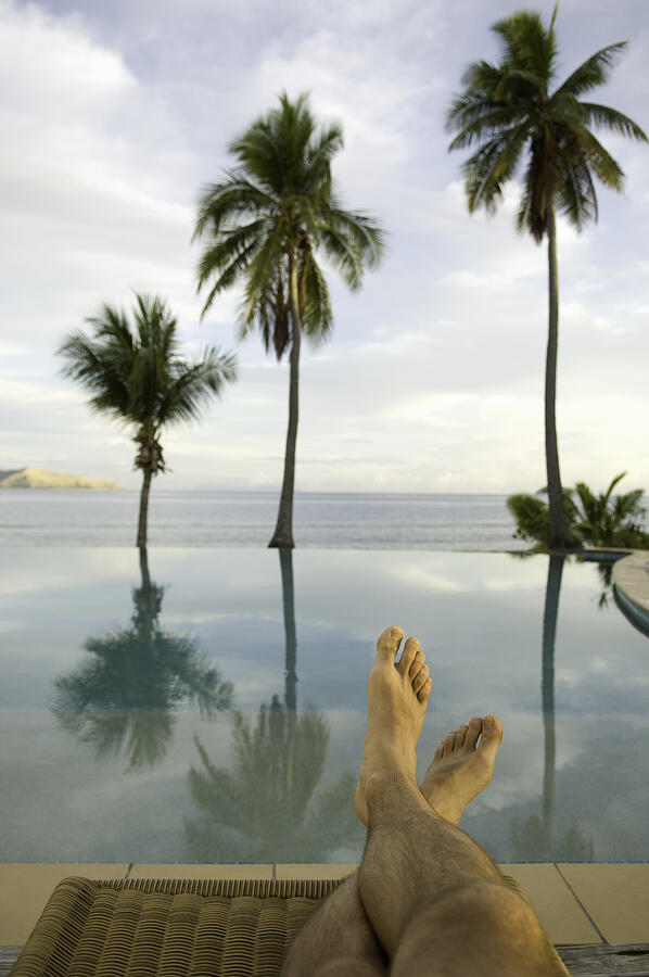 Fiji, man sitting on lounge chair beside infinity pool, low section Photograph by Darryl Leniuk