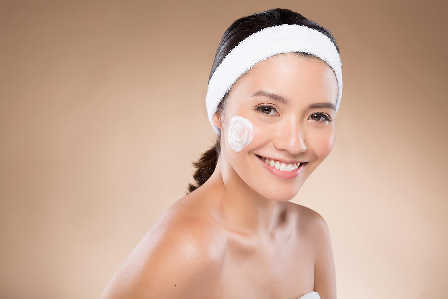 Filipina lady using cream on her face, as part of her skin care routine Photograph by Paper Boat Creative